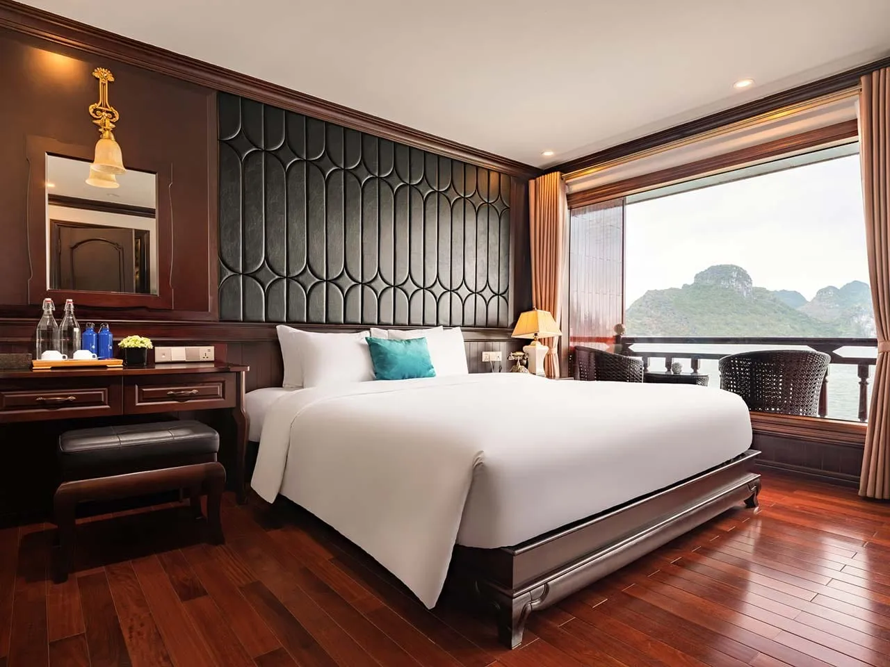 A cruise ship cabin with a bed, decorative headboard, and large window showing limestone karst islands on the water.