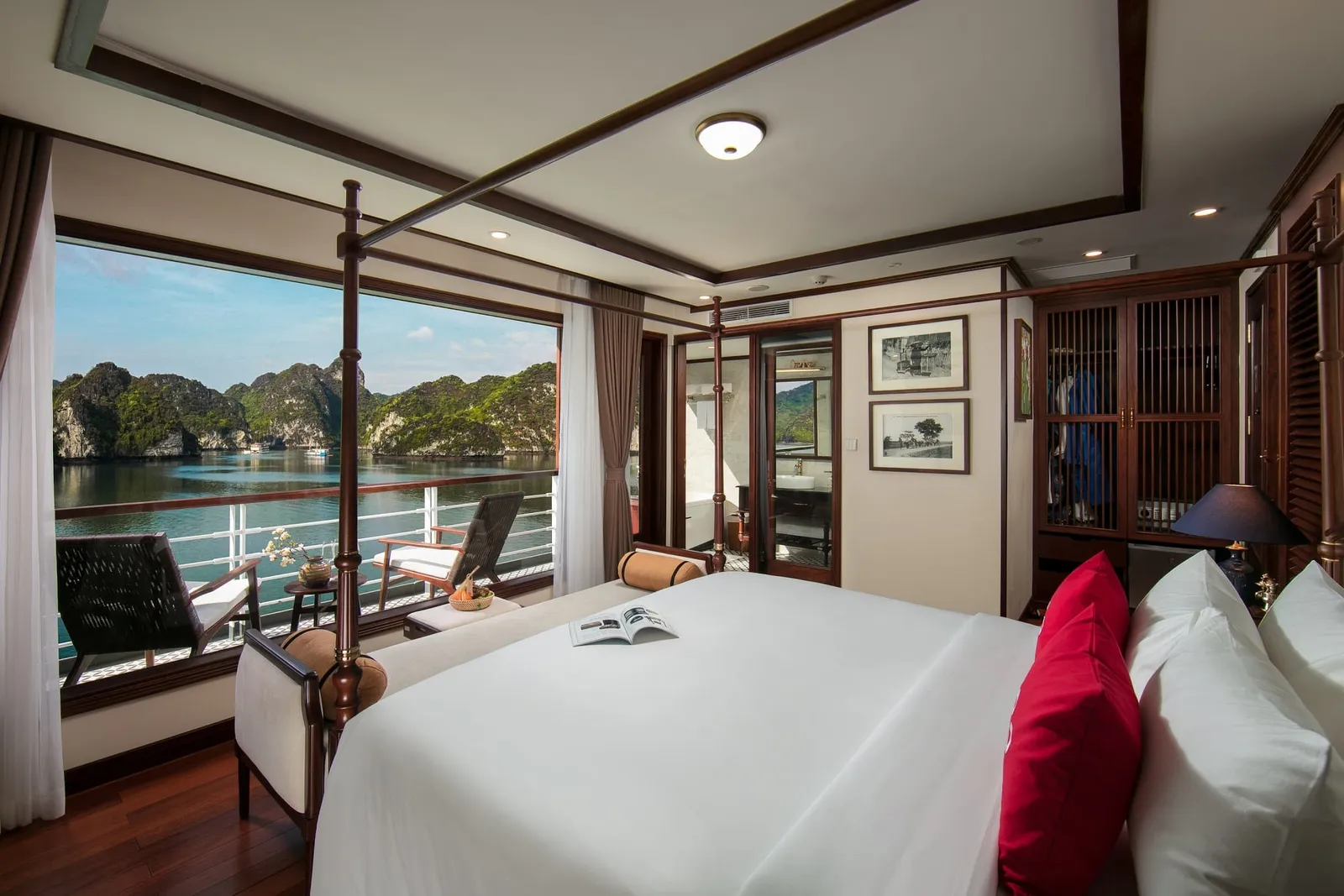 A cruise ship cabin interior with a four-poster bed, private balcony, and limestone karst islands visible through the open door.