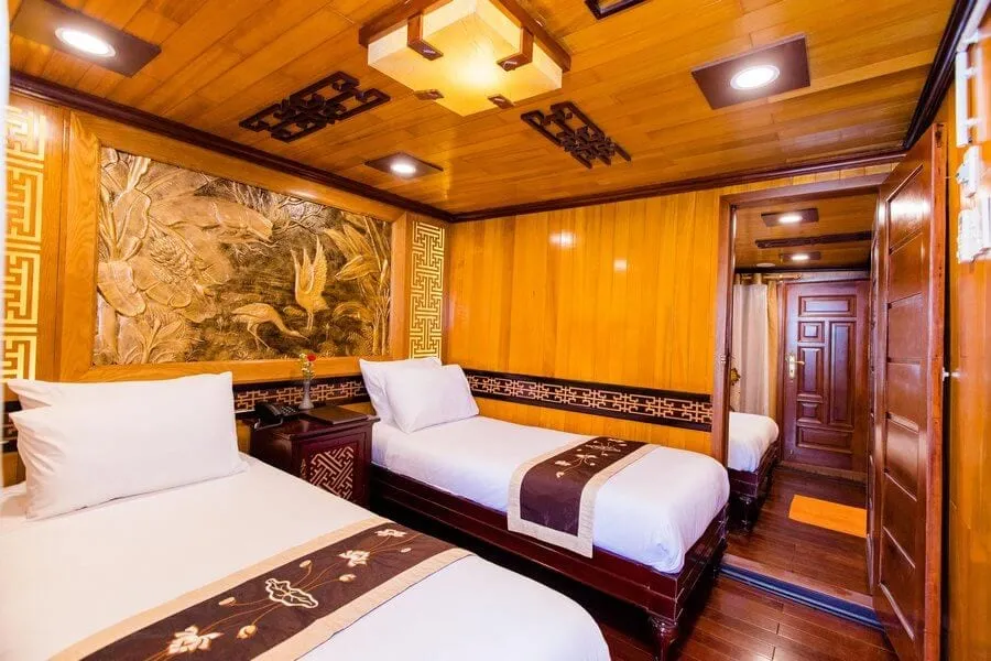 A wooden cabin interior with two beds, decorative carved wall panel, and traditional Asian geometric patterns on the trim.