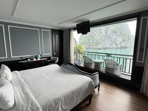 Cabin opening onto a balcony with two chairs, a green cliff filling the window
