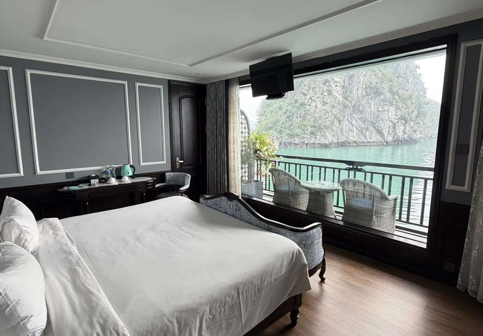 Cabin opening onto a balcony with two chairs, a green cliff filling the window