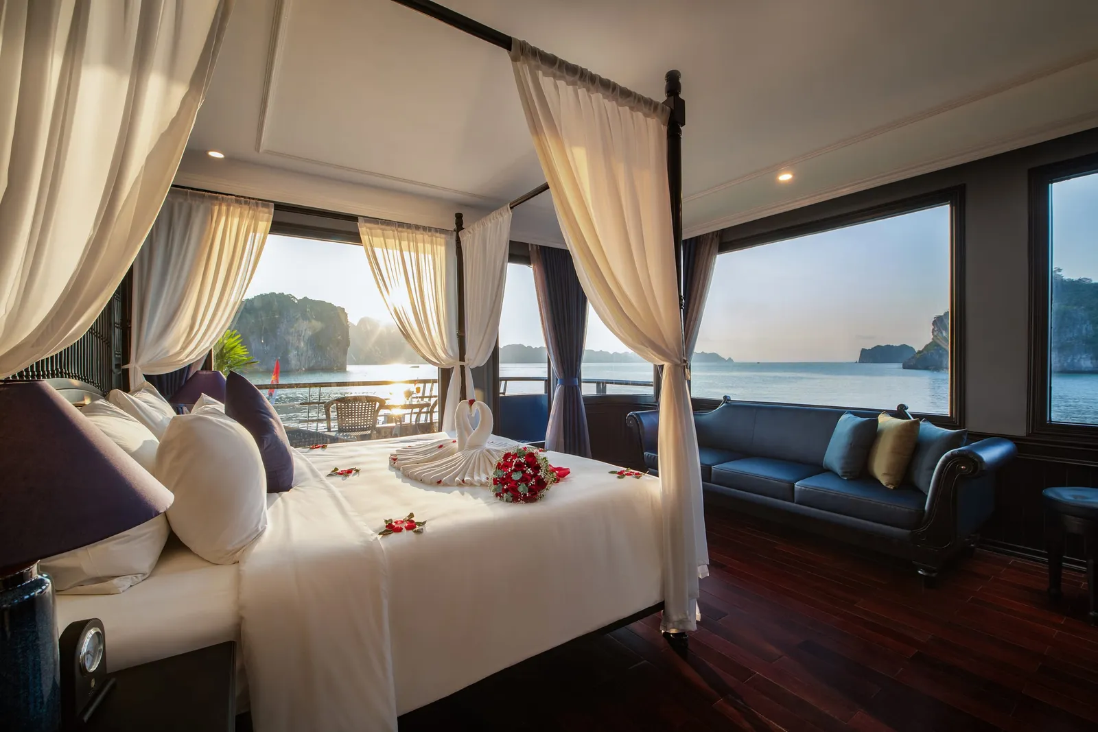 Suite with a canopied bed, a navy sofa under the window and a wall of glass onto the bay
