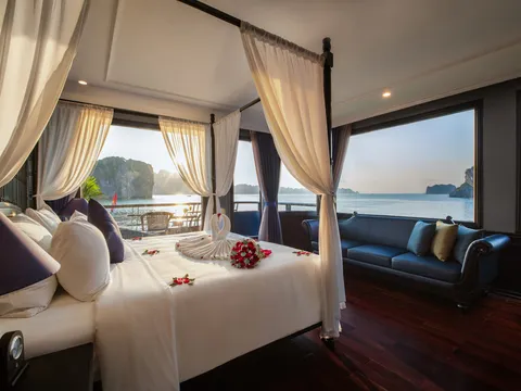 Suite with a canopied bed, a navy sofa under the window and a wall of glass onto the bay