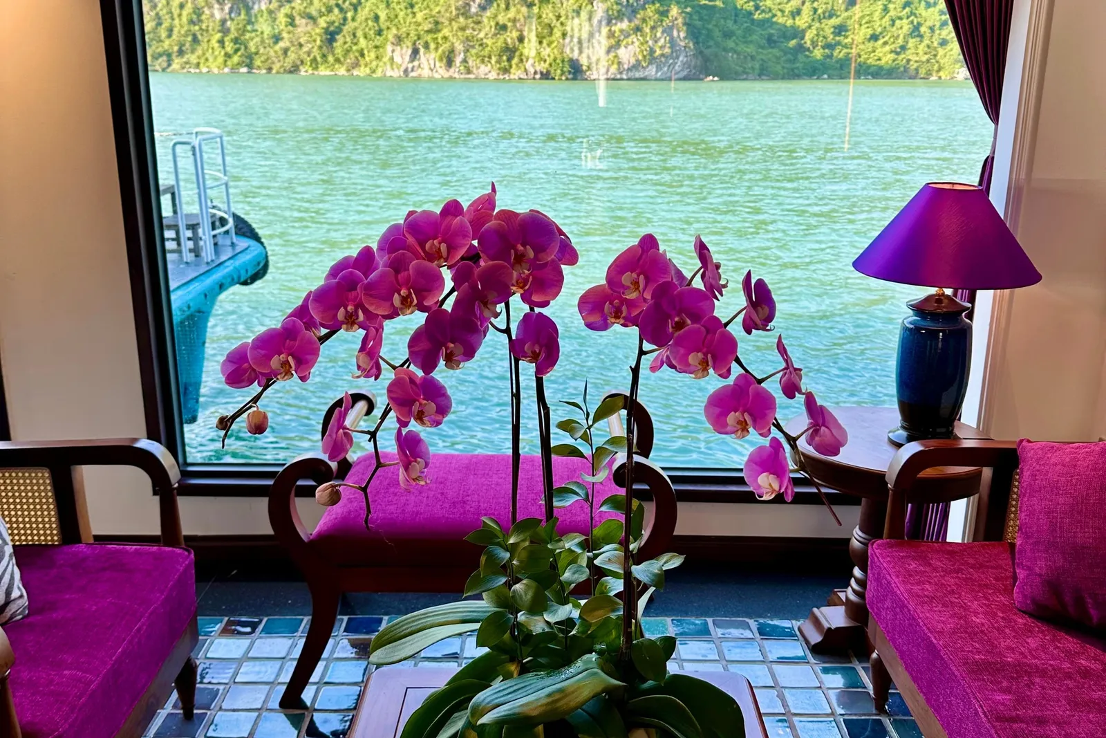 Cabin sitting area with magenta armchairs and orchids on the table, the bay filling the window