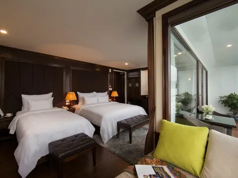 Family cabin with two beds side by side, a bench at the foot and a green cushion on the armchair by the window