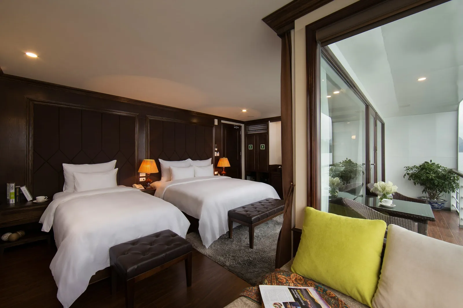 Family cabin with two beds side by side, a bench at the foot and a green cushion on the armchair by the window