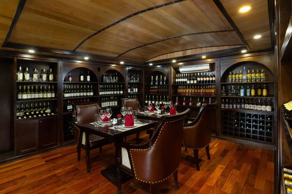 An elegant dining room with curved wooden ceiling, arched wine shelves, a set table with red napkins, and leather chairs on polished wooden flooring.