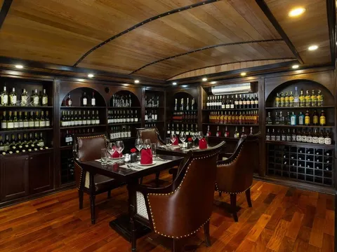 An elegant dining room with curved wooden ceiling, arched wine shelves, a set table with red napkins, and leather chairs on polished wooden flooring.