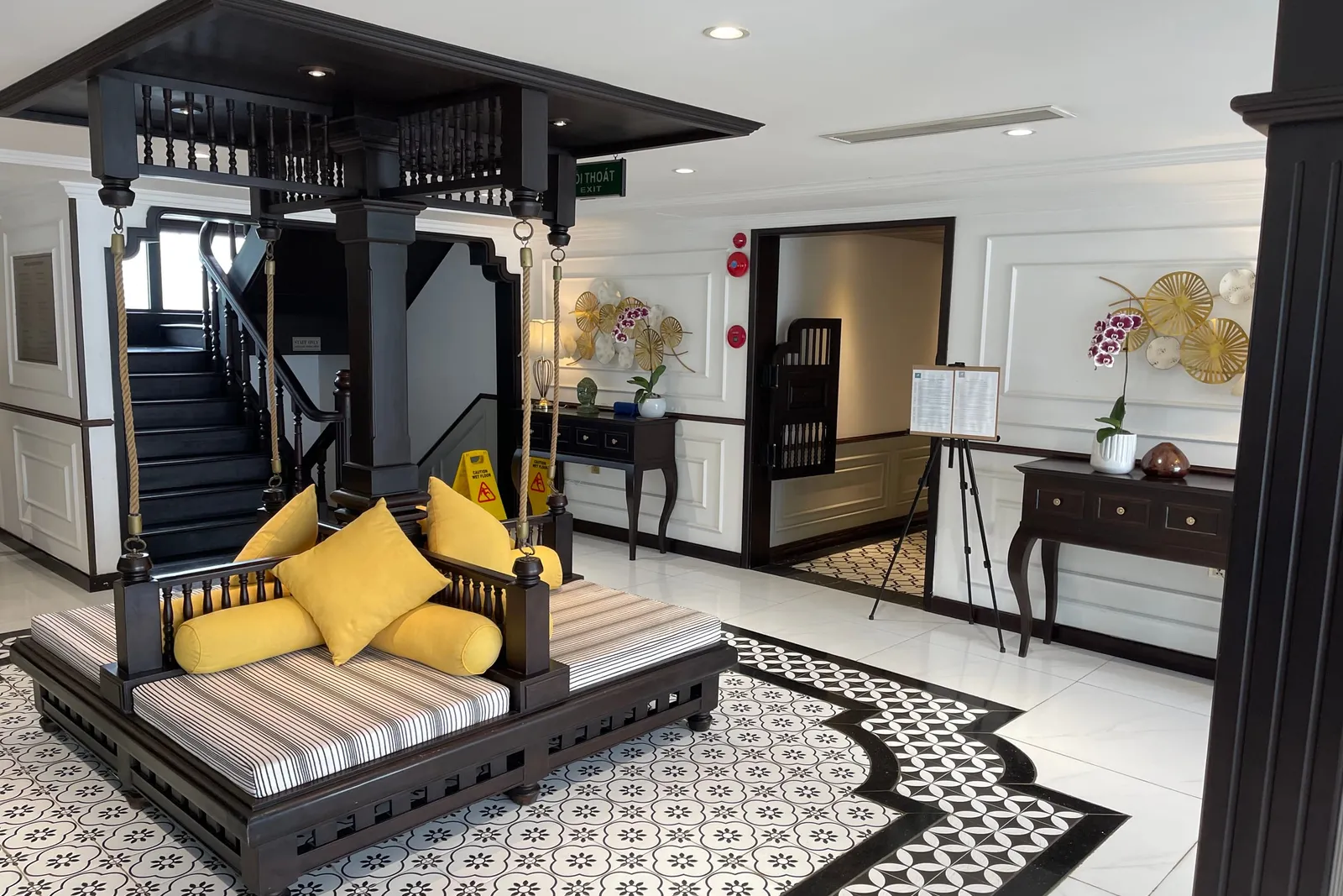 Lounge by the stairwell with a long cushioned bench, yellow bolsters and a black and white tiled floor