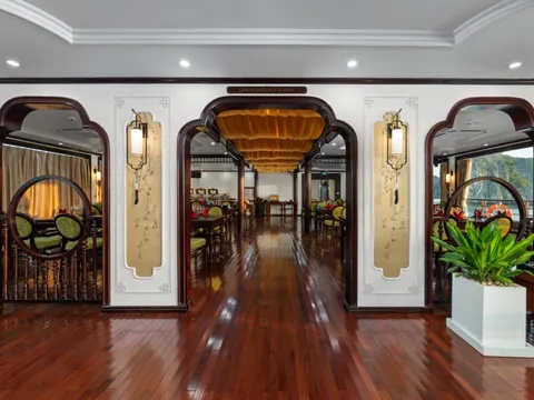 An interior corridor with polished wooden floors, ornate arched doorways with dark wood trim, decorative wall panels with lantern sconces, and circular moon-gate style openings leading to dining areas on either side.