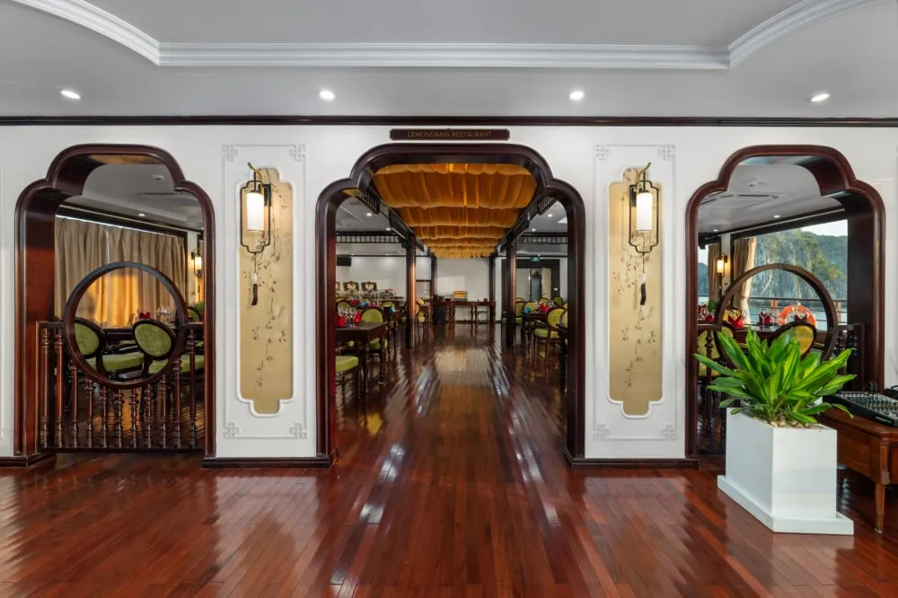 An interior corridor with polished wooden floors, ornate arched doorways with dark wood trim, decorative wall panels with lantern sconces, and circular moon-gate style openings leading to dining areas on either side.