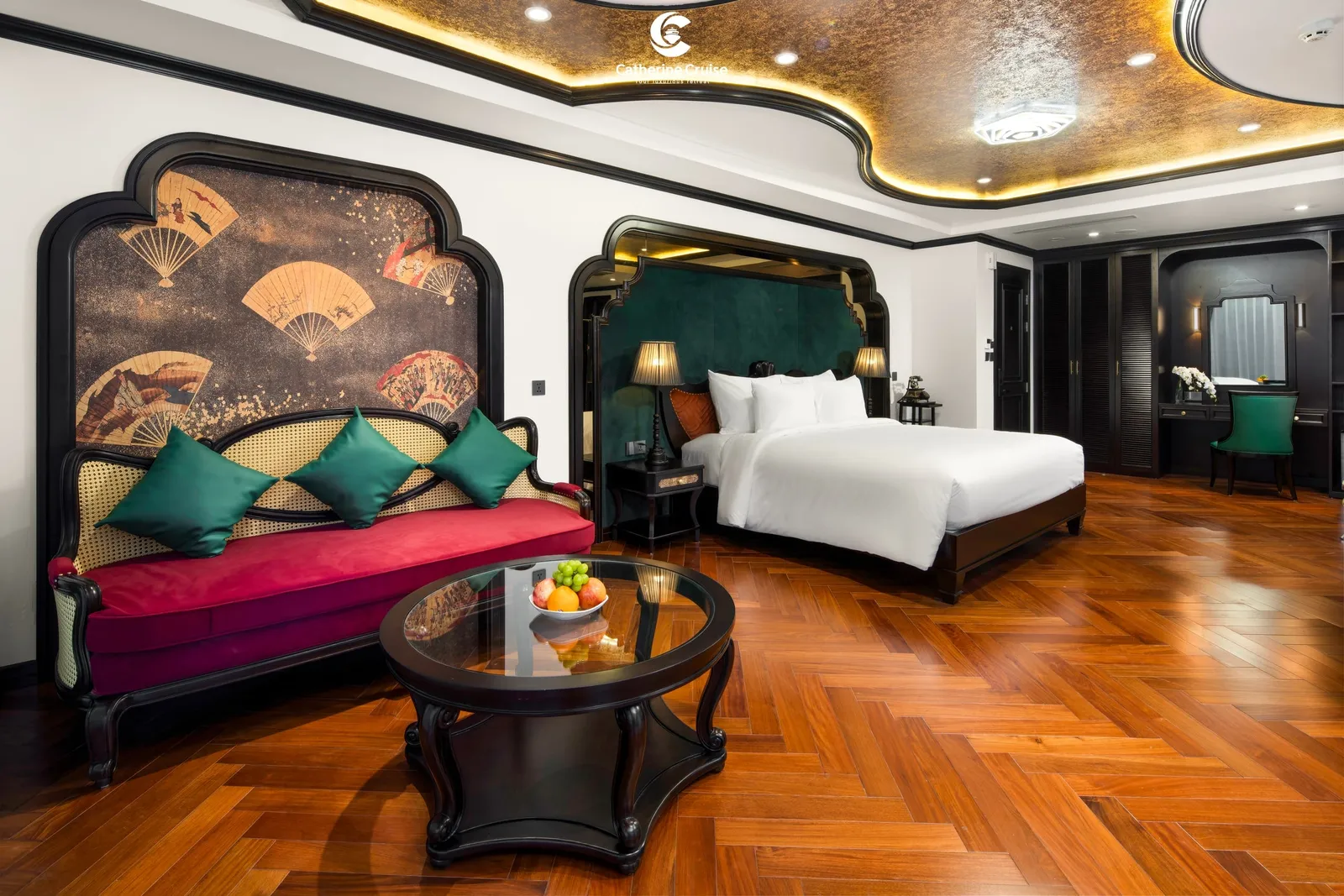 Suite sitting area with a pink sofa and teal cushions under a fan-motif panel, bed beyond on a herringbone floor