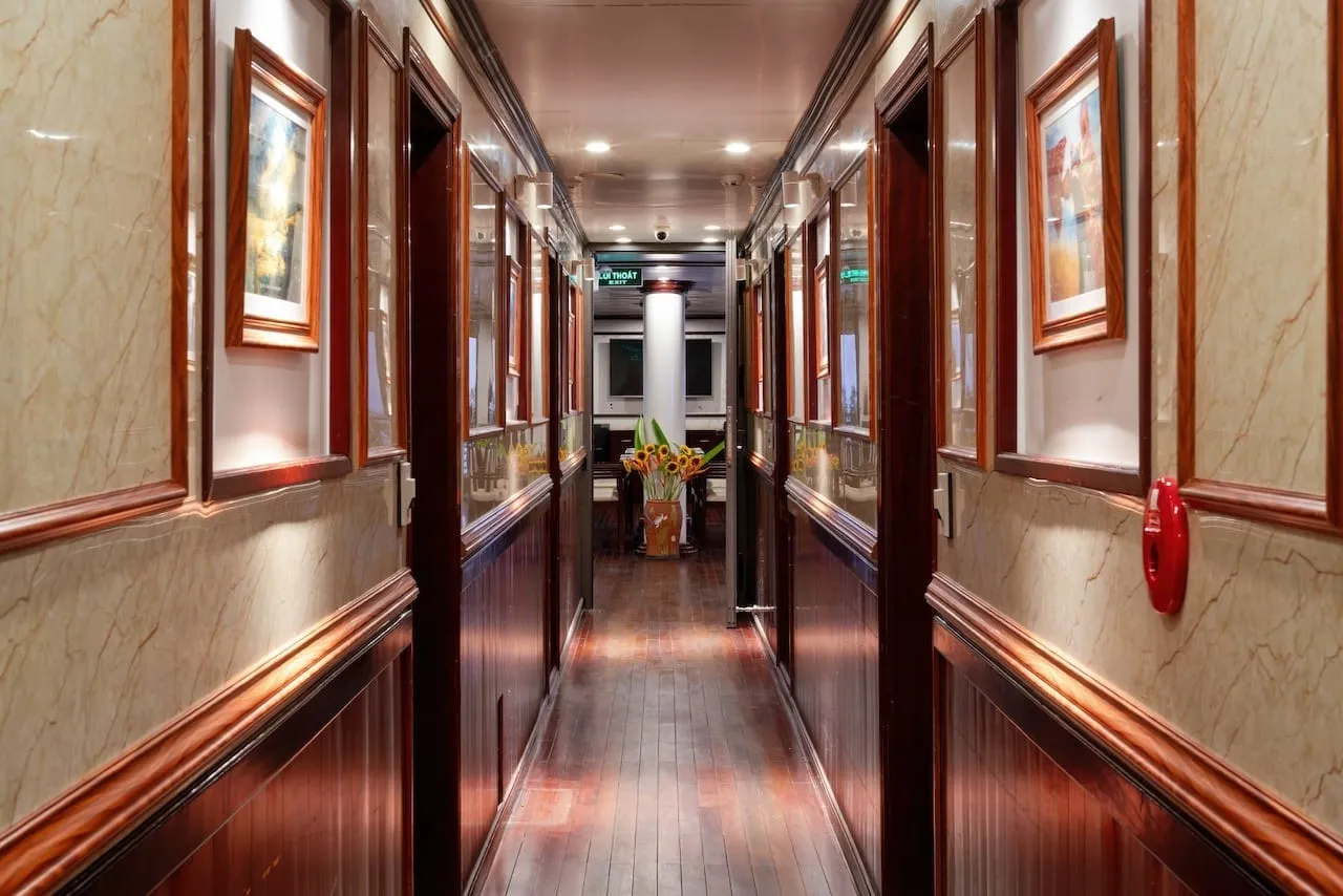 Cabin corridor in marble and dark timber, framed pictures between the doors and a vase at the far end