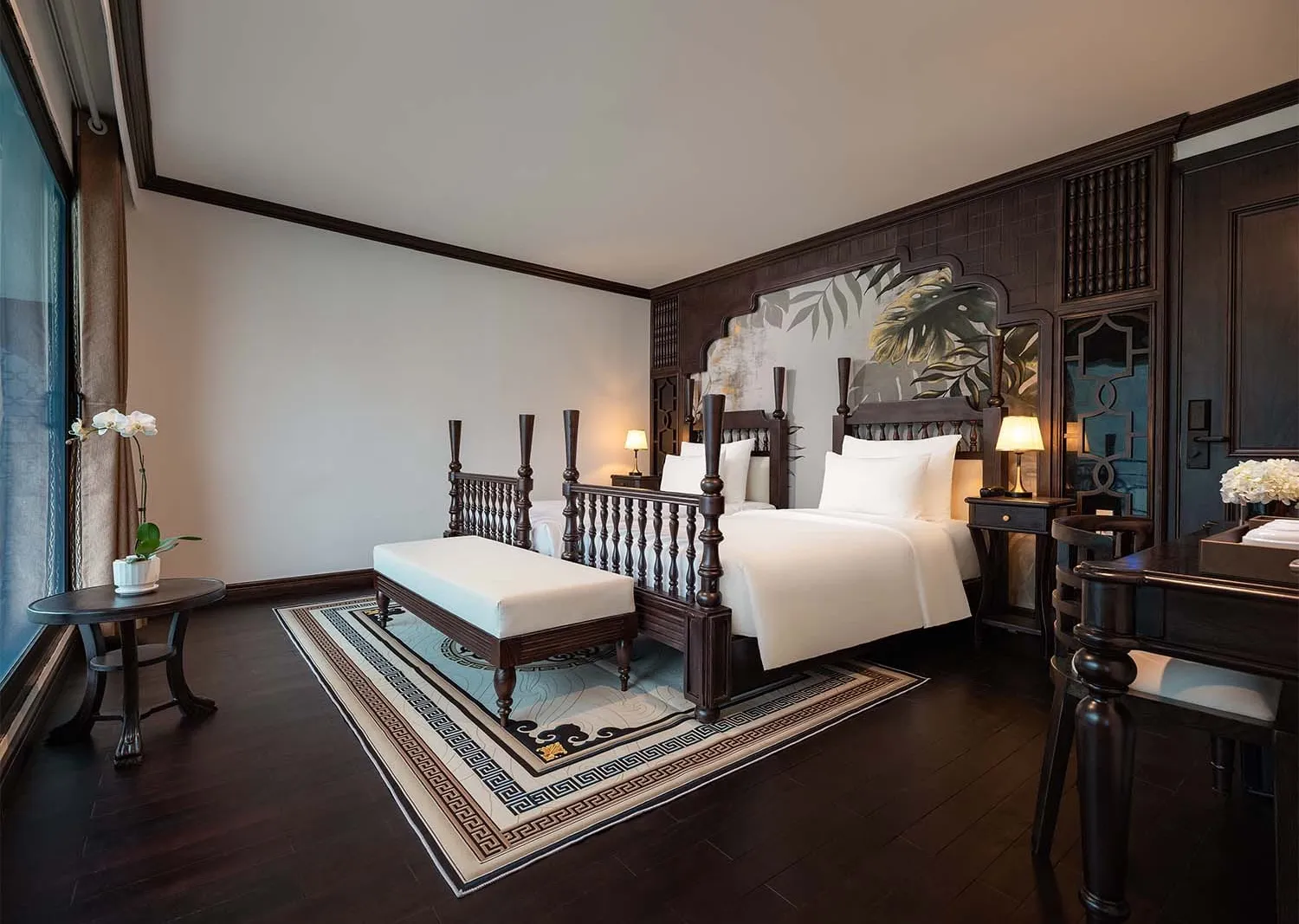 An elegantly furnished cabin bedroom with dark wood paneling, a four-poster bed with white linens, a bench at the foot, bedside lamps, and a patterned area rug on dark hardwood floors.