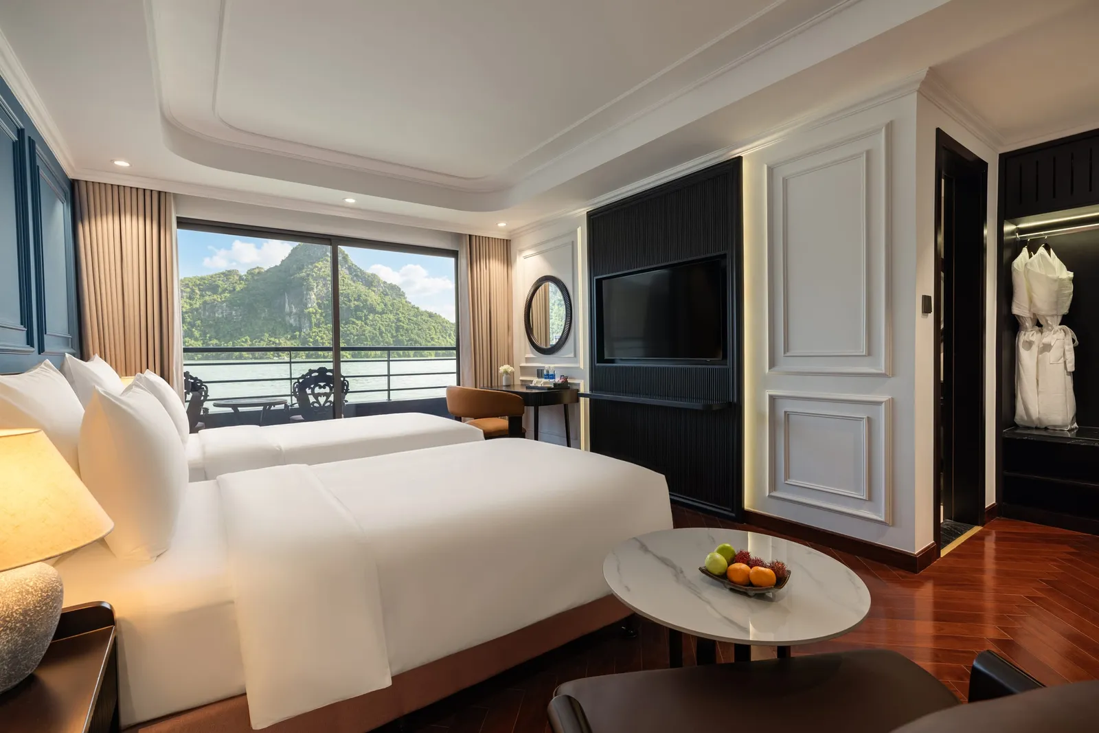 A luxury cabin interior with two beds, dark wood floors, and a large window showing karst mountains and water outside.
