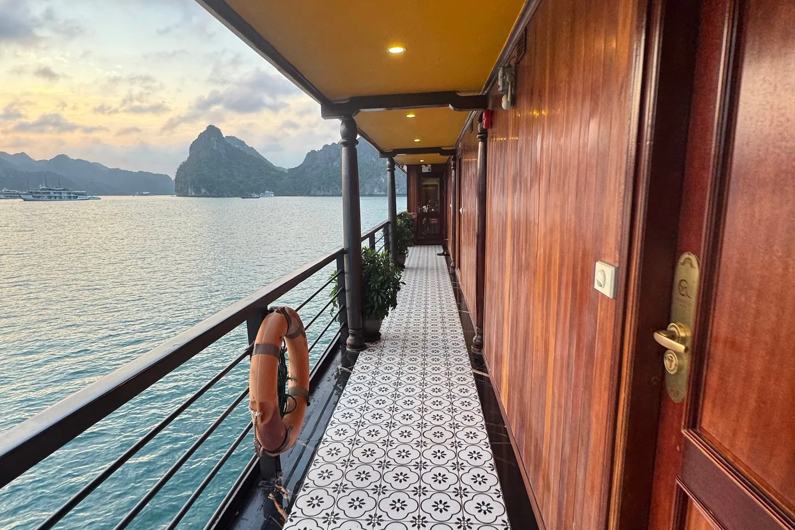 Outside walkway past the cabin doors, a lifebuoy on the rail and patterned tiles underfoot