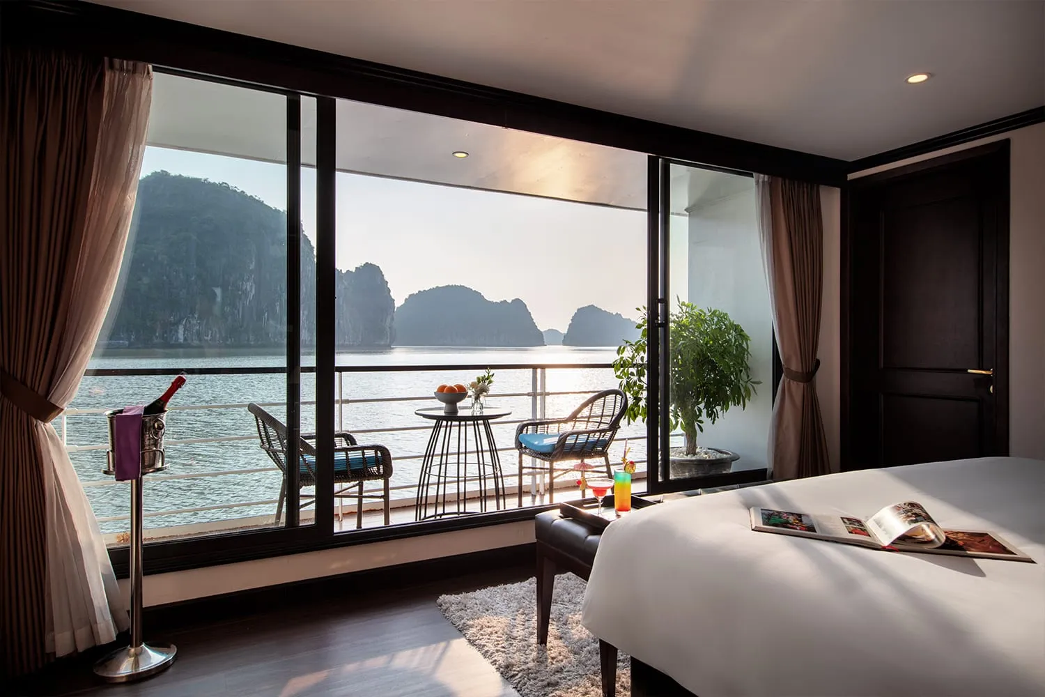 Suite with floor-to-ceiling glass onto the bay, two chairs and a small table set in front of the balcony doors