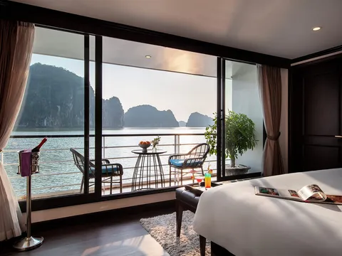 Suite with floor-to-ceiling glass onto the bay, two chairs and a small table set in front of the balcony doors