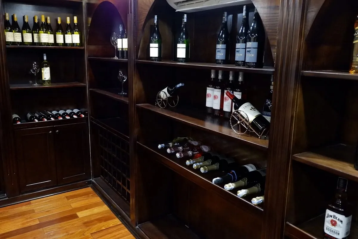 A dark wood wine storage room with built-in shelving displaying wine bottles and decorative holders on polished wooden flooring.