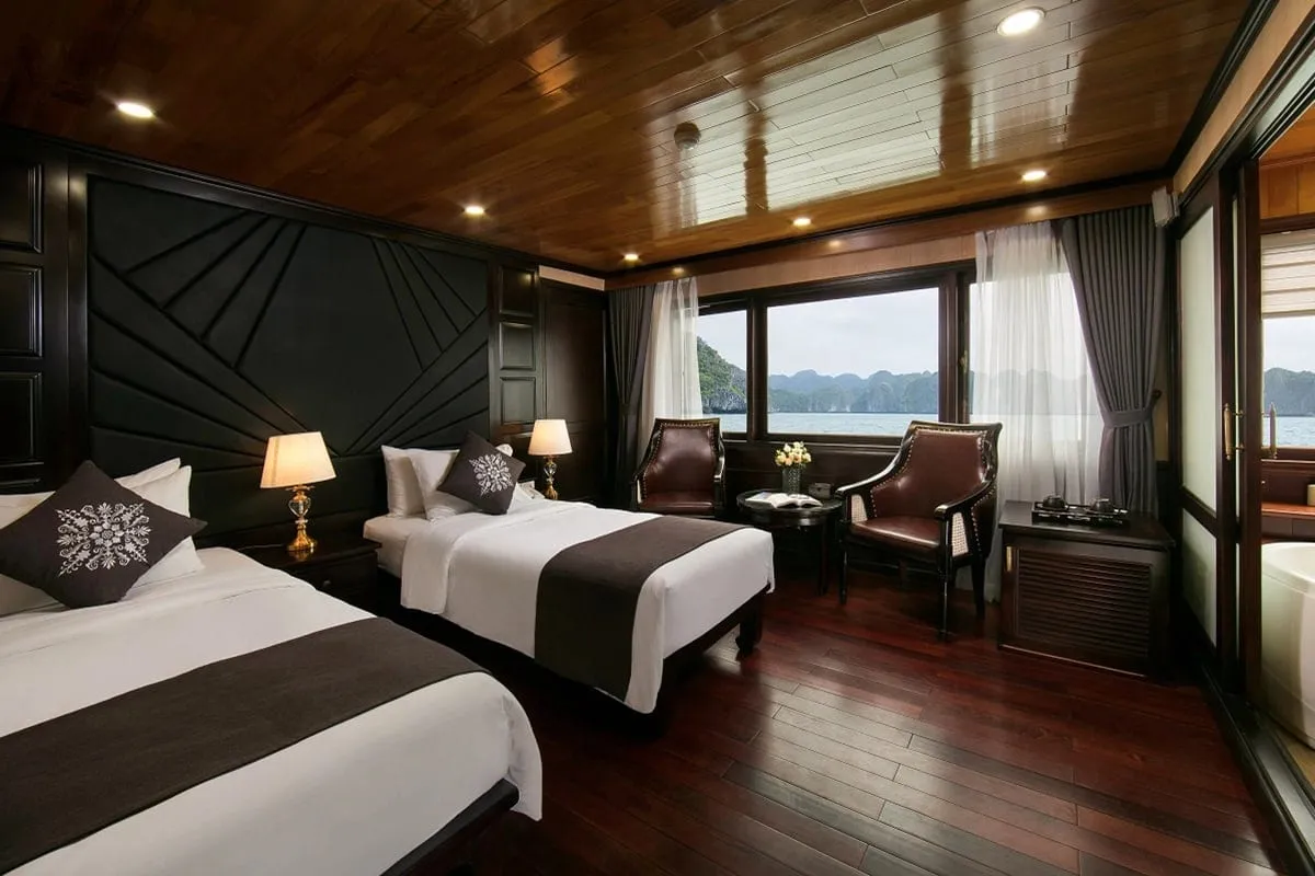 A twin-bed cabin with dark wood paneling, wooden ceiling, and large windows showing karst limestone formations on the water.