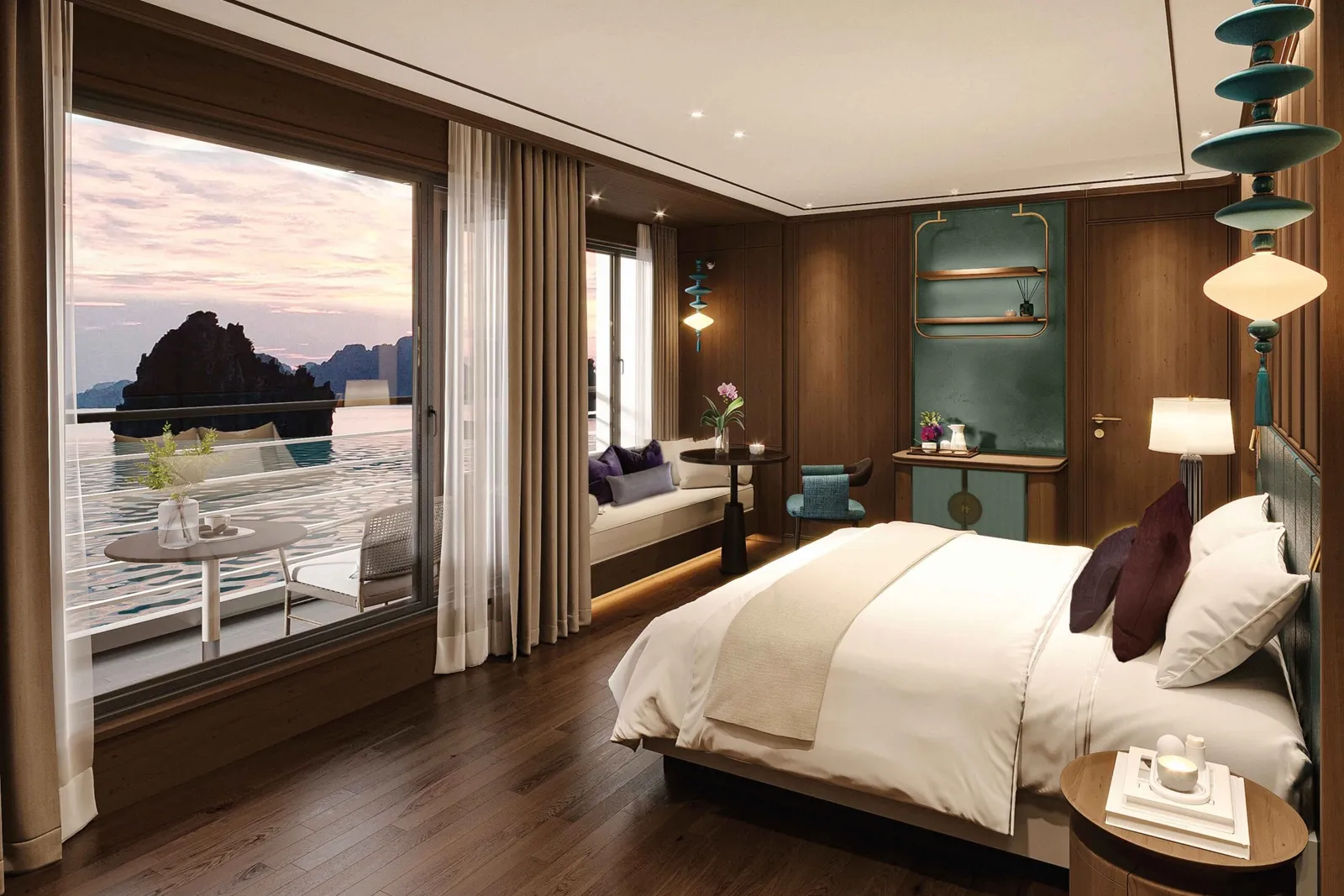 A luxury cabin interior with a bed, wood paneling, and large windows opening to a deck with limestone karsts visible across the water at sunset.