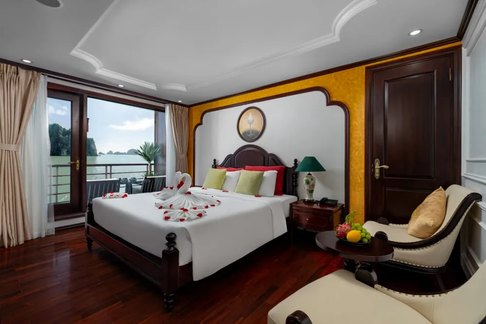 A cruise boat cabin with a bed decorated with towel swans and rose petals, with limestone karsts visible through the window.