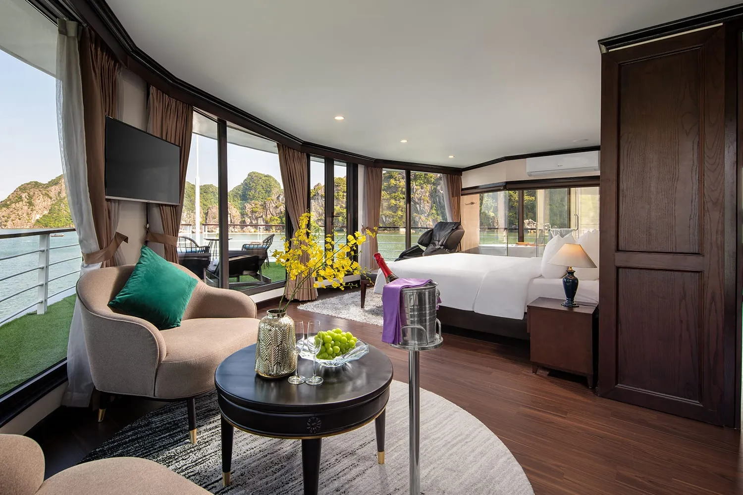 Suite living area with a sofa, a low round table and a television on the panelled wall, bed behind