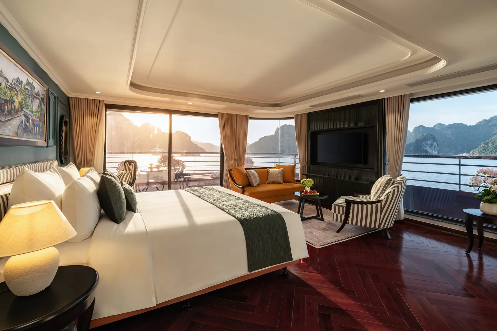A luxury cabin interior with a bed, orange sofa, and large windows showing limestone karsts and water outside.