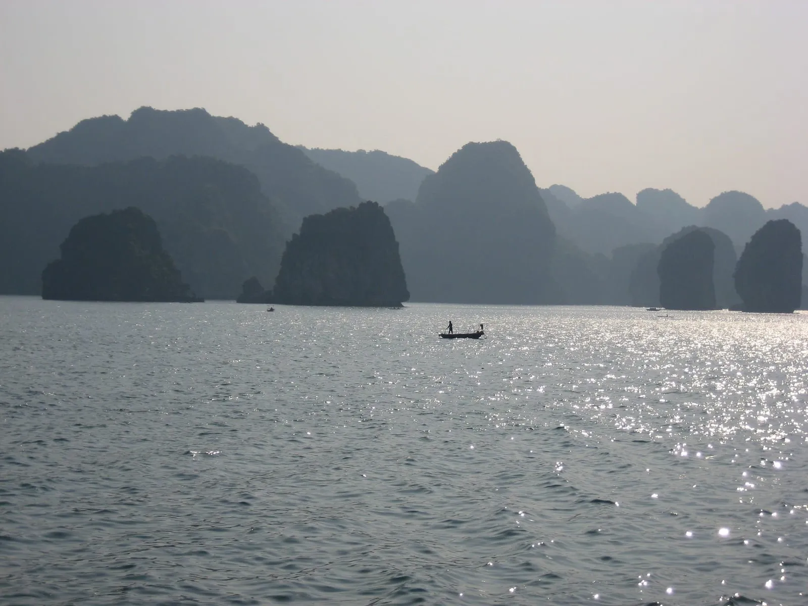 Limestone islands under a hazy sky, with a small boat on the water