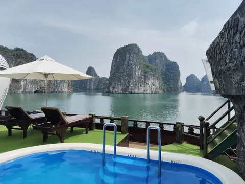 Deck pool with sun loungers under a white umbrella, the rail and open bay just beyond