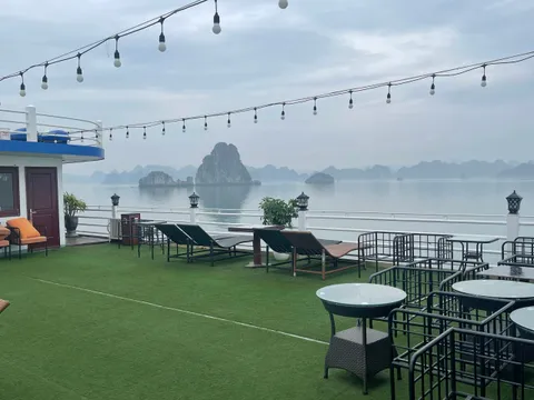 Sundeck laid with green matting, loungers and cafe tables under a run of string lights, karst beyond the rail
