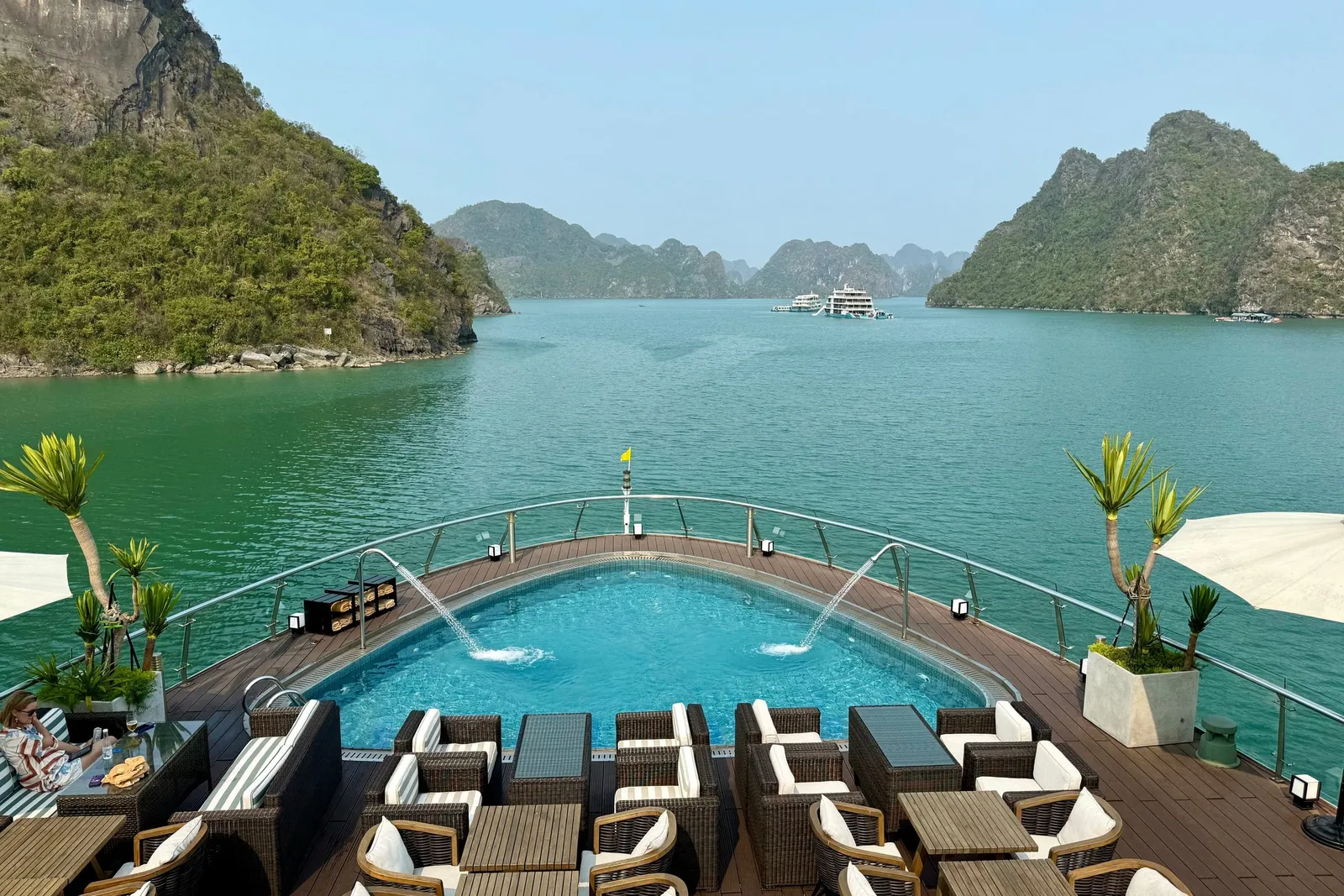 Sundeck pool with loungers along both sides and potted palms at the rail, the bay opening out beyond