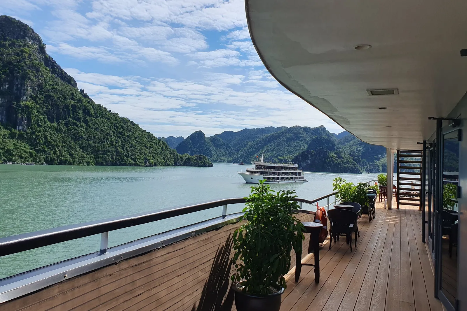 Timber deck with potted plants and a table at the rail, another cruise boat passing across the bay