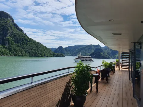 Timber deck with potted plants and a table at the rail, another cruise boat passing across the bay