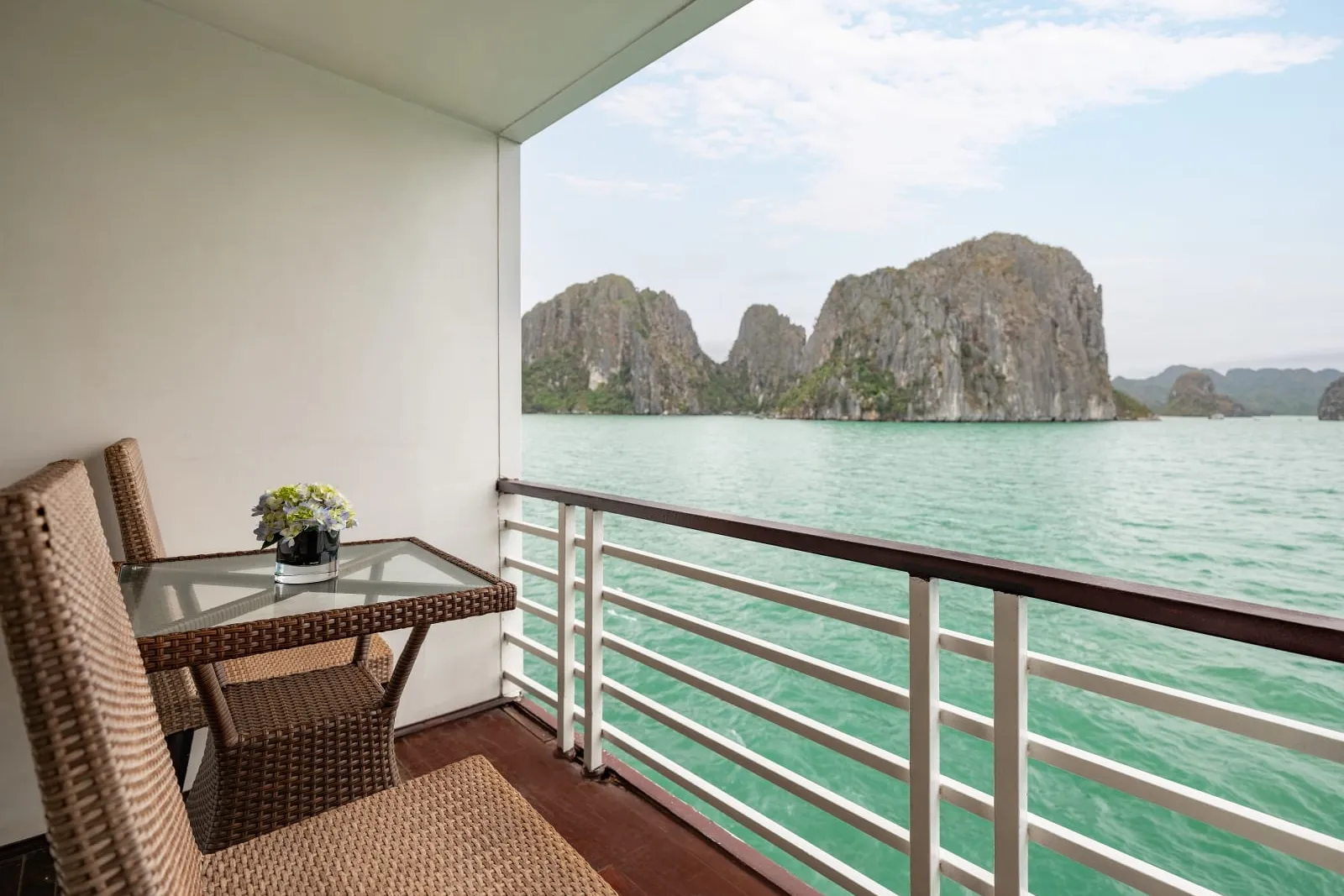 A private balcony with wicker furniture overlooking turquoise water and dramatic limestone karst formations.
