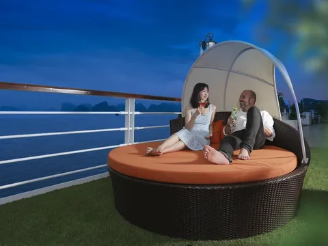 Canopied round daybed on the sundeck with two guests sitting on it, the rail and open water behind