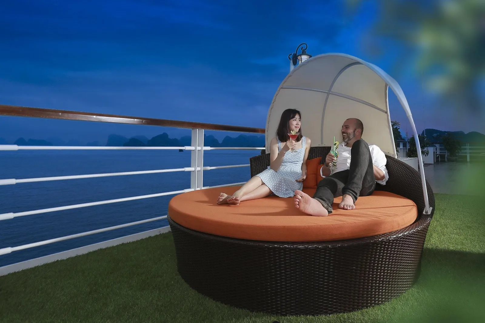 Canopied round daybed on the sundeck with two guests sitting on it, the rail and open water behind