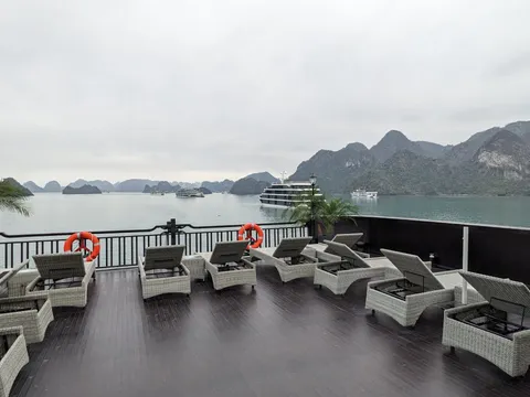 Sundeck laid with rattan loungers behind a dark rail, another cruise boat at anchor across the channel