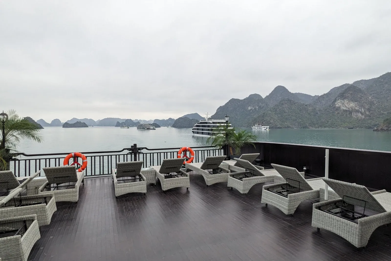 Sundeck laid with rattan loungers behind a dark rail, another cruise boat at anchor across the channel