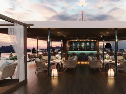 A sunset-lit cruise boat deck with a bar, lounge seating, and dramatic karst islands visible through open sides.