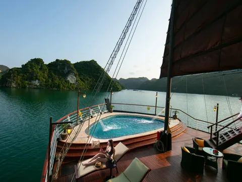 A wooden deck with a circular jacuzzi, lounge furniture, and staff member, with limestone karst islands in calm water behind.