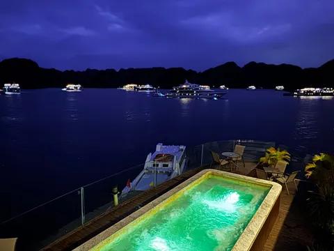 Deck pool lit green after dark, chairs set around it and the lights of other boats out on the water