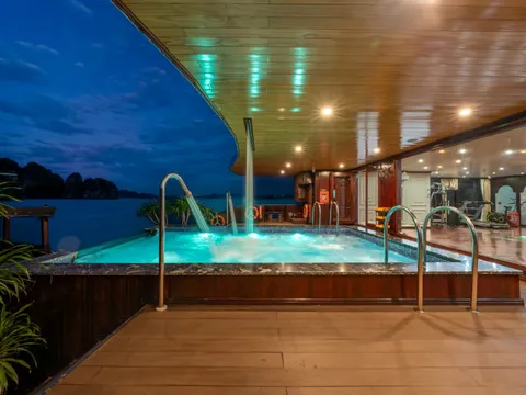 A wooden deck with an illuminated hot tub at twilight, overlooking calm waters with limestone karsts visible in the distance.