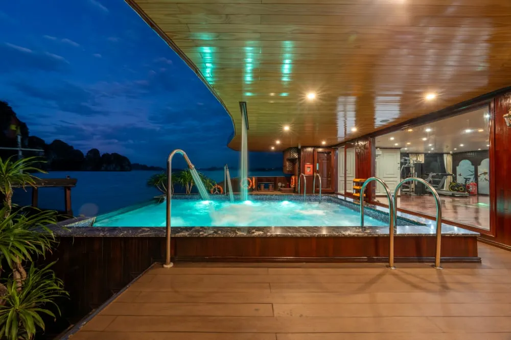 A wooden deck with an illuminated hot tub at twilight, overlooking calm waters with limestone karsts visible in the distance.