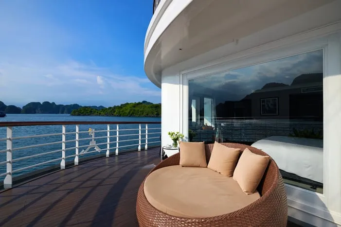 A deck with a round wicker daybed and cushions overlooks blue water with limestone karsts in the background.
