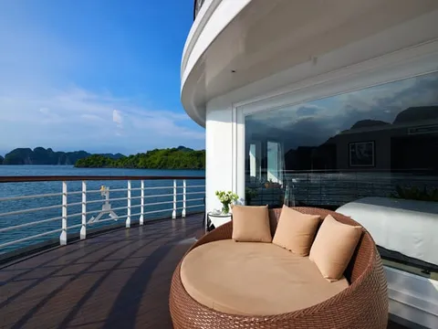 A deck with a round wicker daybed and cushions overlooks blue water with limestone karsts in the background.