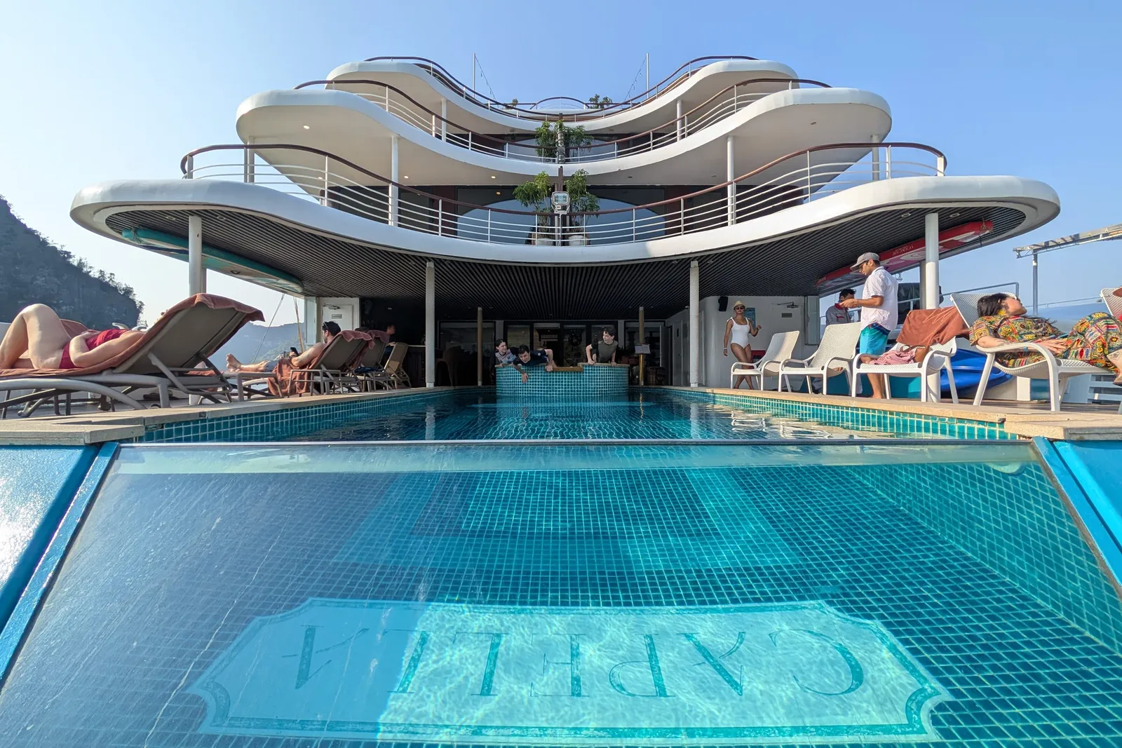 Sundeck pool with the ship name set into the tiled floor, loungers along both sides and the curved white superstructure above