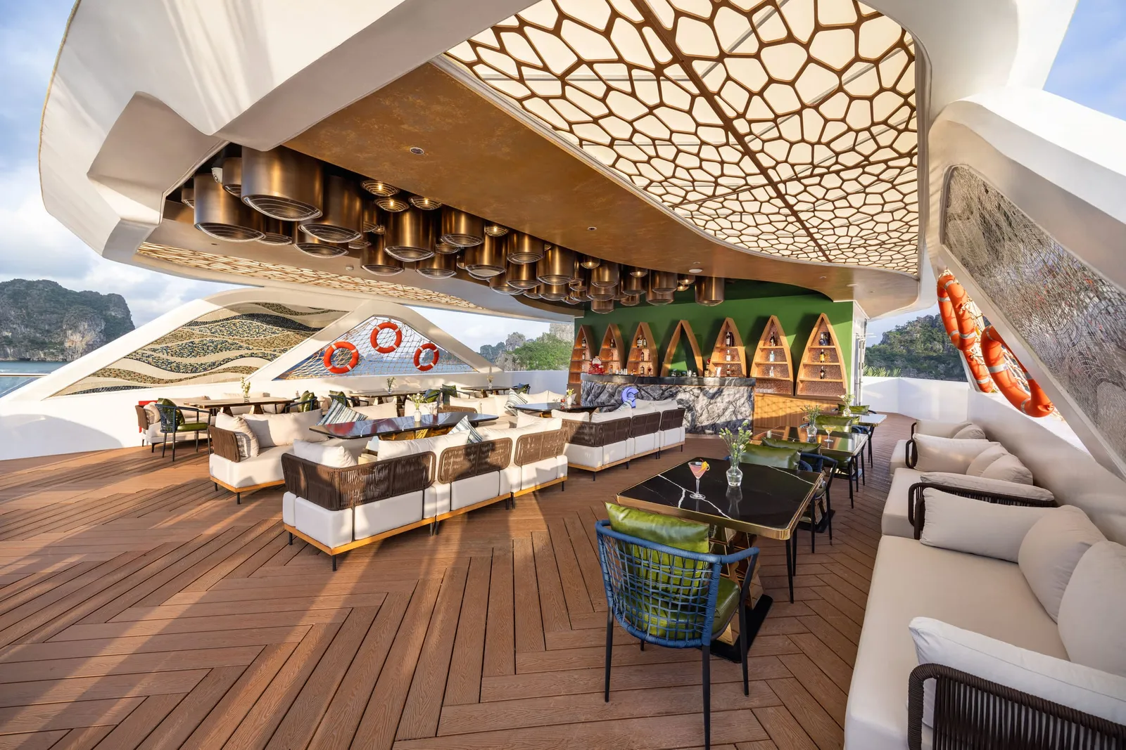 Open-air lounge under a honeycomb canopy, low sofas and a timber deck running out to the rail