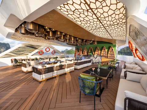 Open-air lounge under a honeycomb canopy, low sofas and a timber deck running out to the rail