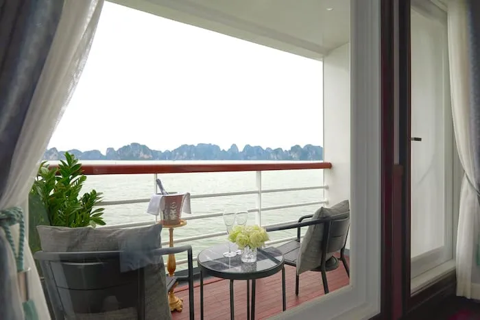 A private balcony with chairs and a small table overlooking calm waters with limestone karst formations in the distance.